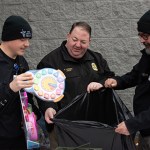 Med Center Health Advanced EMT Benjamin McCarty, Warren County Jailer Stephen Harmon and Warren County Regional Jail Sergeant Joseph Blair place a donation into a bag of toys at the Toys for Tots' Hand It To A Hero event Saturday at the Walton Avenue Walmart.