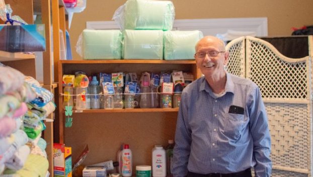 Picture of Don Fricks, executive director of the Pregnancy Support Center of Bowling Green, standing beside shelves of supplies for pregnant mothers and their babies.