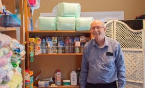 Picture of Don Fricks, executive director of the Pregnancy Support Center of Bowling Green, standing beside shelves of supplies for pregnant mothers and their babies.